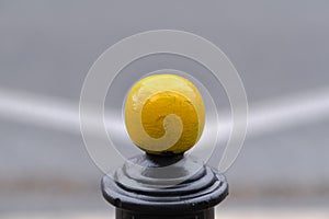 Single yellow metal ball on street post, blurred street