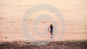 A singular semi silhouetted surfer bobs in morning waters off lighthouse point