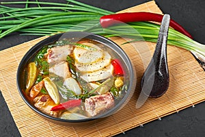 Sinigang na Baboy dish or Filipino Pork Meat Soup in black bowl on dark slate backdrop. Filipino Food. Asian Meal photo