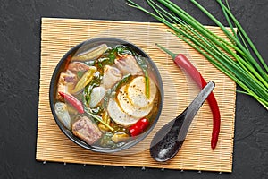 Sinigang na Baboy dish or Filipino Pork Meat Soup in black bowl on dark slate backdrop. Filipino Food. Asian Meal photo