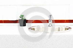 The sink in the bathroom on the background of bright tiles with a bright stripe, the design of a flower in a pot