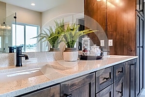 Sink and faucet of bathroom with wood cabinets and window reflected on mirror