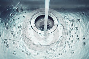 In the sink in the kitchen, water flows from the tap, which flows into the drain hole