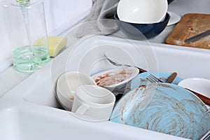 Sink with many dirty utensils and dishware in messy kitchen