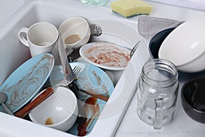 Sink with many dirty utensils and dishware in messy kitchen