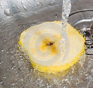 In the sink for running water and a slice of yellow Apple.