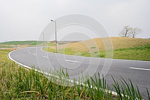 Sinuous asphalted road on grassy acclivity in light winter mist