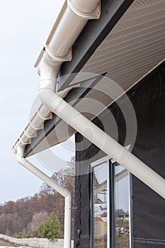 SIP panel house construction. New white rain gutter. Drainage System with Plastic Siding Soffits and Eaves against blue sky.