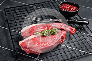 Sirloin steak or Cap Rump, raw beef meat with herbs on a rack. Black background. Top view