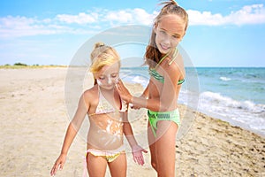 Sister applying protective sunscreen on child. Girl draws sun cream on her stomach