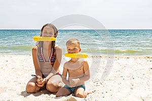 Sister and brother holding corn cobs in their mouth on the sea beach. Summer street eating concept