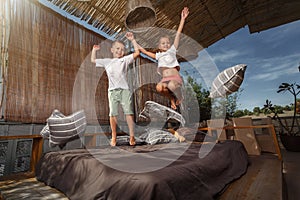 Sister and brother jumping on the bed, playing and laughing on veranda