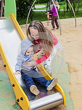 Sister and brother playing on the Playgrou. The girl helps a little boy on a children`s slide.