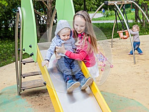 Sister and brother playing on the Playgrou. The girl helps a little boy on a children`s slide.