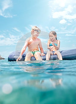 Sister and brother sitting on inflatable mattress and enjoying the sea water, cheerfully laughing when swim in the sea. Careless