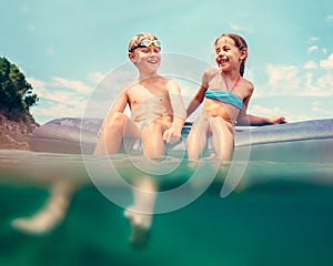 Sister and brother sitting on inflatable mattress and enjoying the sea water, cheerfully laughing when swim in the sea. Careless