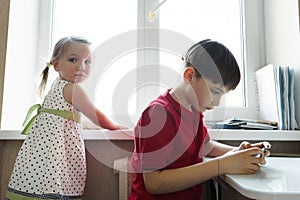 Sister and brother are sitting in the kitchen and playing with the phone