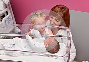 The sister and grandmother looks at a newborn baby in the hospital