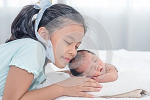 Sister happy welcome her little brother. Toddler kid meeting new sibling. Cute girl and new born baby boy relax in a white bedroom
