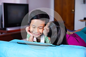 Sister kissing her brother on the cheek while they using tablet.