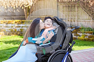 Sister kissing and hugging disabled little brother in wheelchair