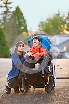 Sister next to disabled little brother in wheelchair outdoors photo