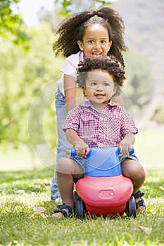 Sister pushing brother on toy with wheels smiling