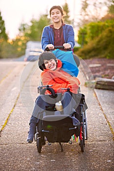 Sister pushing disabled little brother in wheelchair around neighborhood