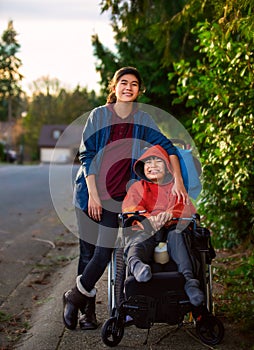 Sister standing next to disabled little brother in wheelchair outdoors