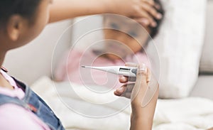 Sister touching her brother`s forehead, checking temperature and holding glass of water