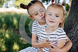 The sister wants to kiss her little sister. Happy kids playing in summer park