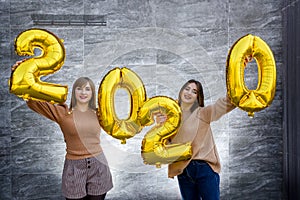 Sisters celebrating new 2020 year. They holding golden air balloons at party celebration