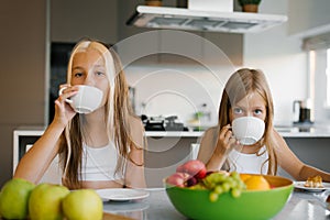 Sisters children have breakfast with tea and fruit in the kitchen