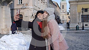 Sisters couple bloggers taking selfie, making video conferencing call on mobile phone on city street