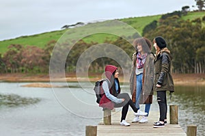 Sisters at heart. a group of friends having a conversation on a pier by a lake.