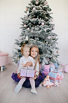 Sisters at home with Christmas tree and presents. Portrait of happy children girls with Christmas gift boxes and decorations.