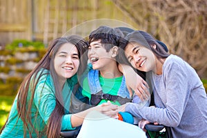 Sisters laughing and hugging disabled little brother in wheelchair outdoors