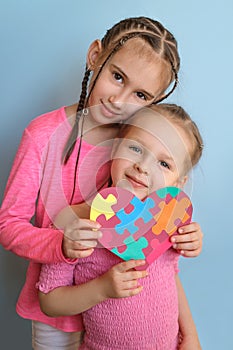 Sisters with pigtails look with smile at the camera holding the autism symbol