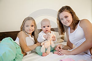 Sisters play with the baby on the bed in the bedroom