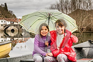 Sisters sitting in the boat on the river and holding the umbrella