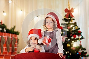 Sisters twins child in Christmas hats Santa with gifts near the