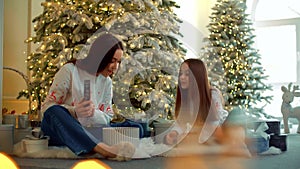 Sisters unwrap gifts while sitting by the Christmas tree