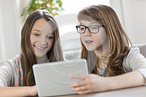 Sisters using digital tablet at table in house