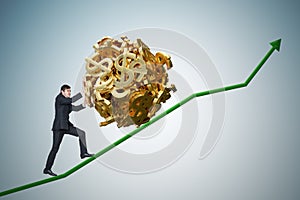 Sisyphus metaphore. Young businessman is maximizing earnings and pushing heavy boulder made of dollar symbol up on chart