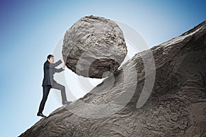 Sisyphus metaphore. Young businessman pushing heavy stone boulder up on hill