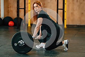 Sitting with barbell on the floor. Beautiful strong woman is in the gym