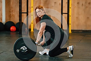 Sitting with barbell on the floor. Beautiful strong woman is in the gym