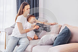 Sitting on the bed with vacuum cleaner part. Mother with her little daughter is indoors at home together