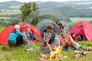 Sitting by campfire friends in tents chatting