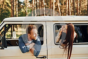 Sitting in the car. Young couple is traveling in the forest at daytime together